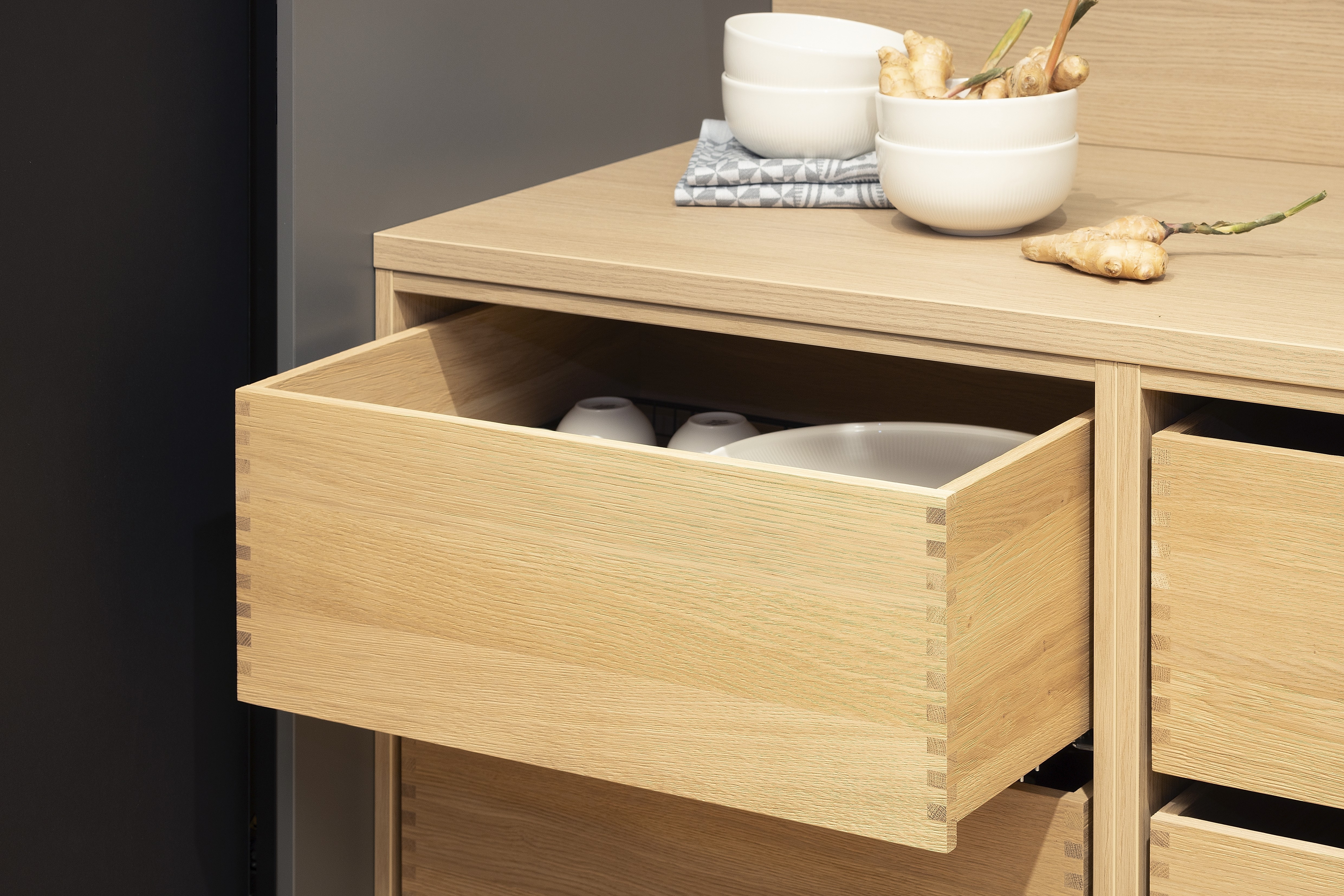 APL: Feineiche-natur Repro 25 mm Front: AV 7080 Schwarz Linoleum Korpus: Designkorpus Feineiche-natur Repro Griff: PTO Kehlleiste Graphit gebürstet Geräte: SMEG  Features: Linoleum Front, Ordnungssystem Boxen, Teeküche, Einschubtüren (Pocket Door System von Häcker) + Unterschrankregale mit Massivholzauszügen